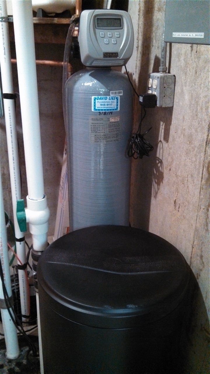 A Water Filter Is Sitting Next To A Black Tank In A Basement | Wichita, KS | David Lies Plumbing