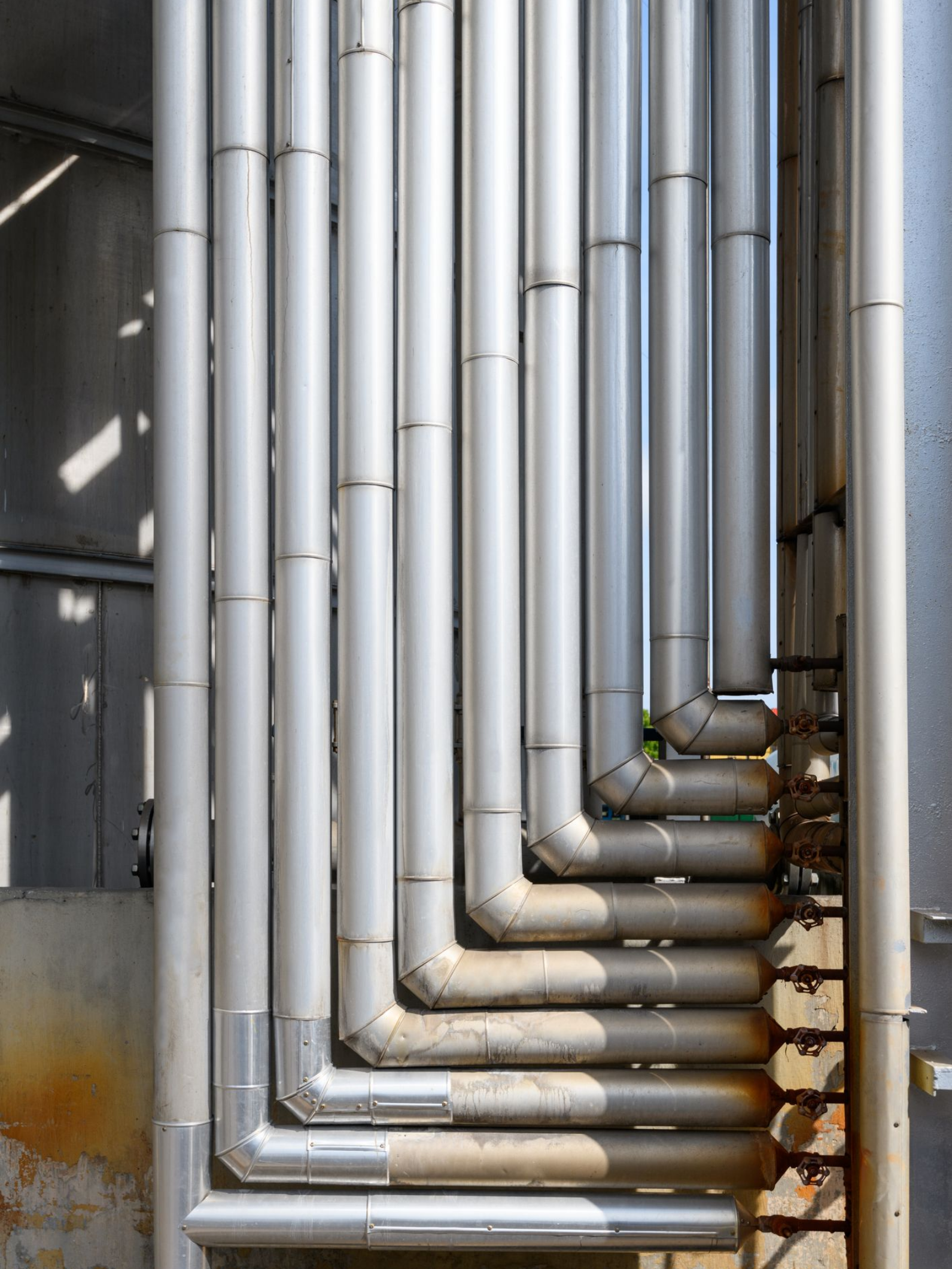 Silver industrial pipes with elbows, clustered on a concrete wall. Silver industrial pipes with elbows, clustered on a concrete wall.