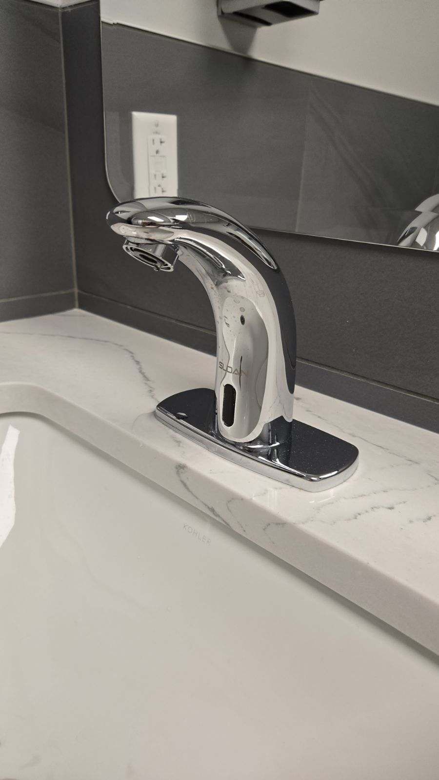 Silver, touchless faucet mounted on a white countertop in a bathroom.