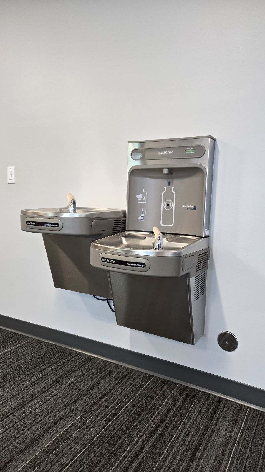Wall-mounted water fountain with bottle filler and a lower accessible fountain, gray and silver.
