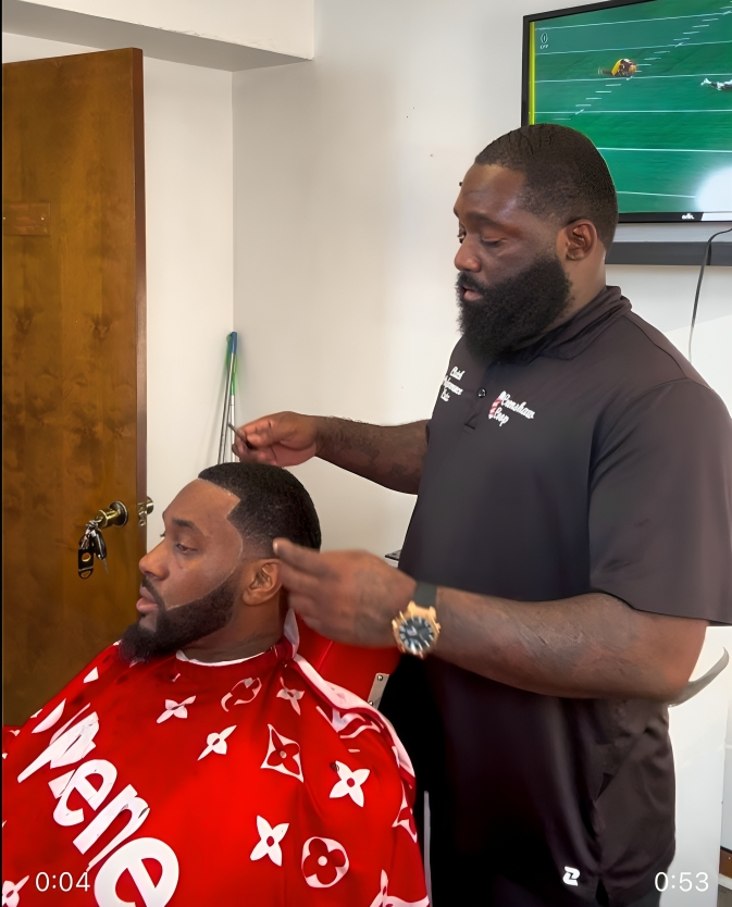 A man is getting his hair cut by a barber wearing a supreme cape