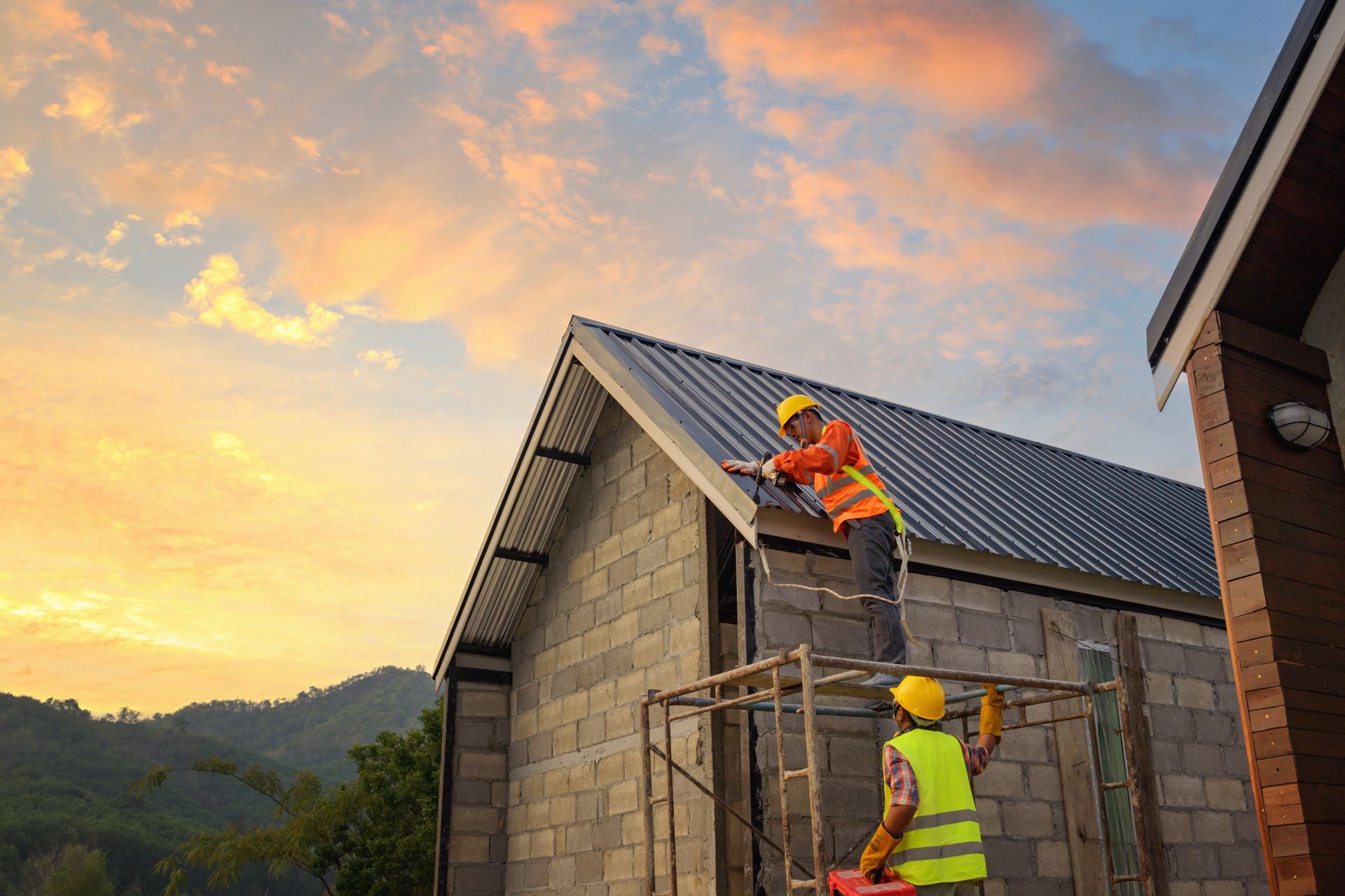 Two construction workers are working on the roof of a house.