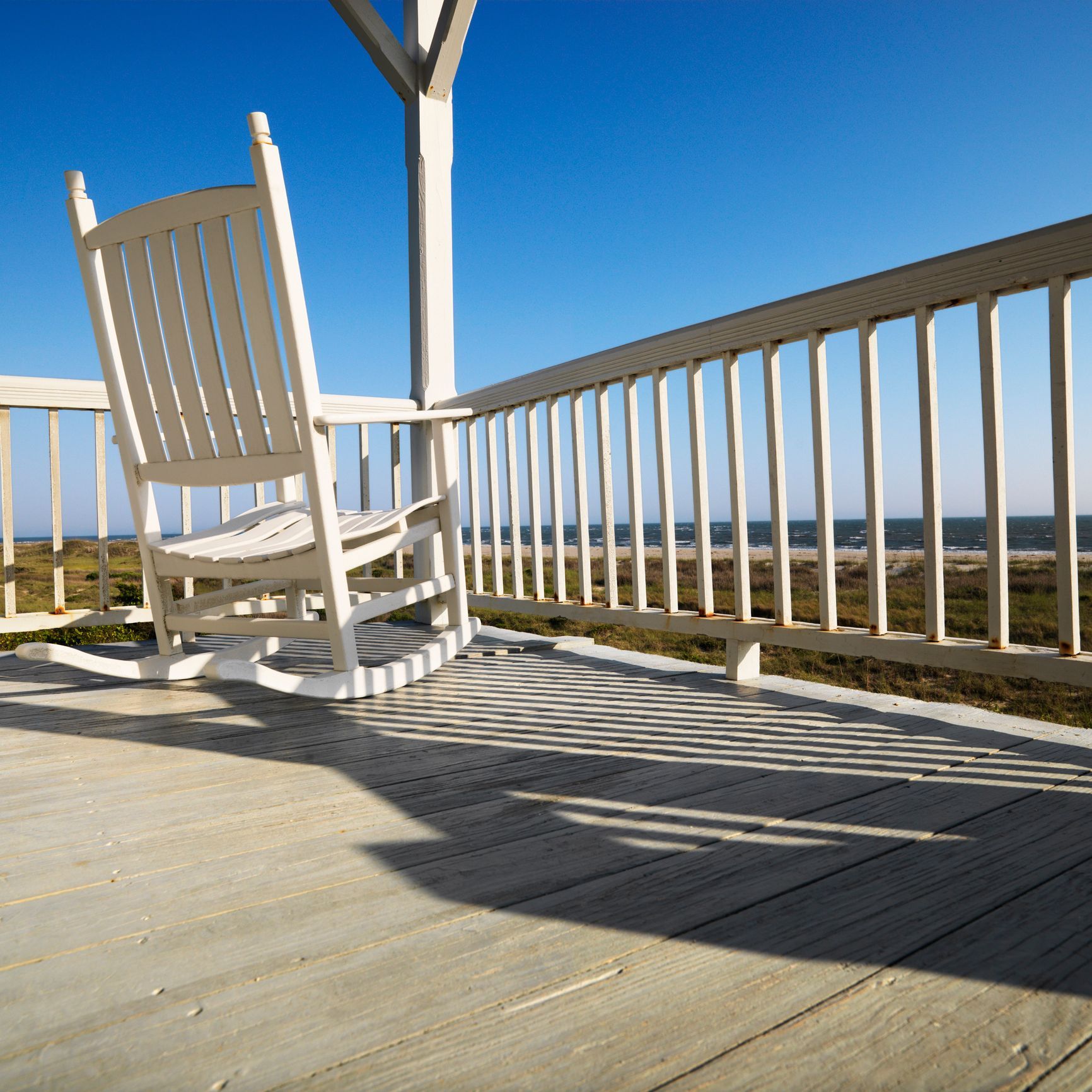 A white rocking chair sits on a deck overlooking the ocean