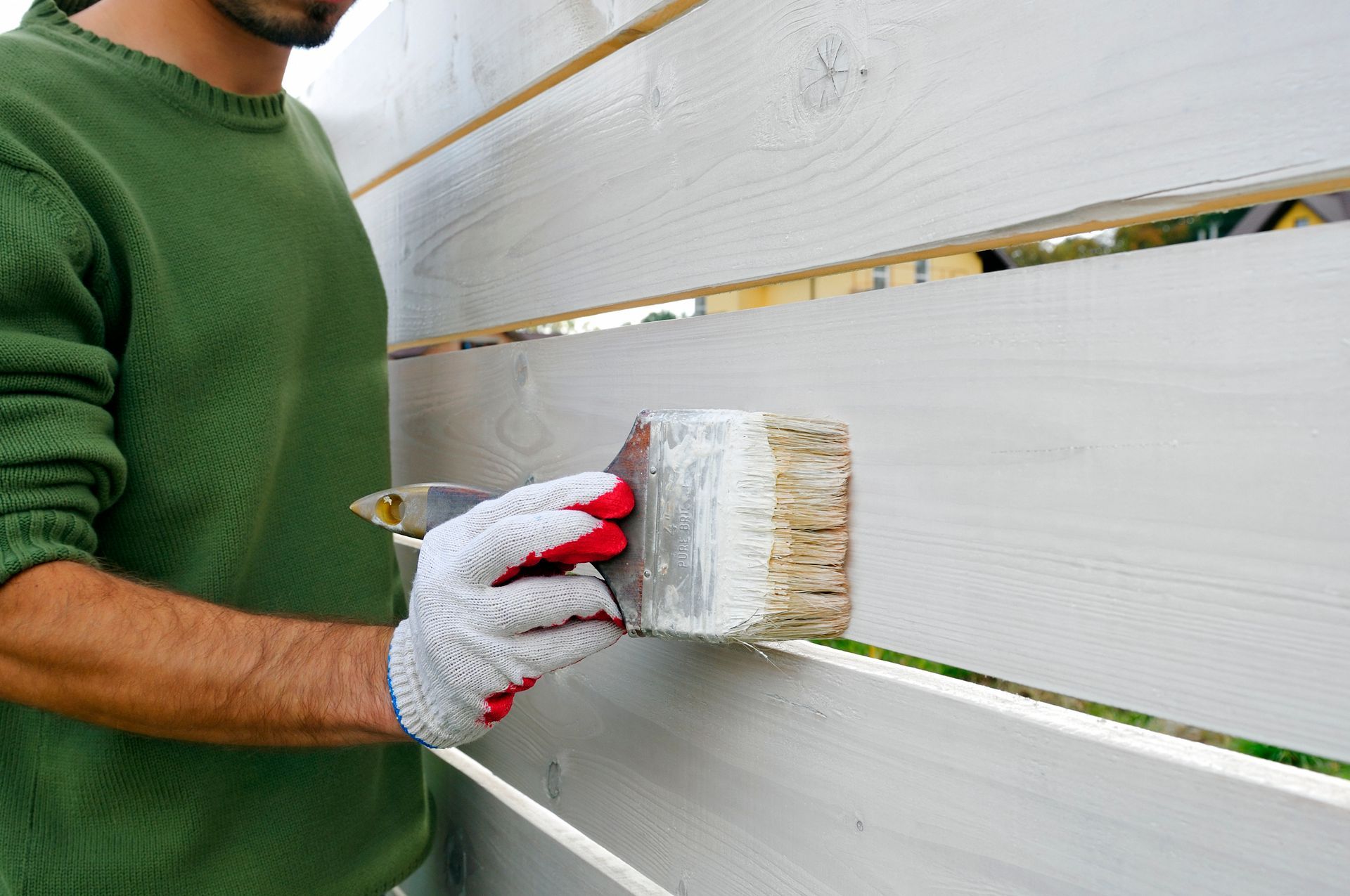 A man is painting a wooden fence with a brush.