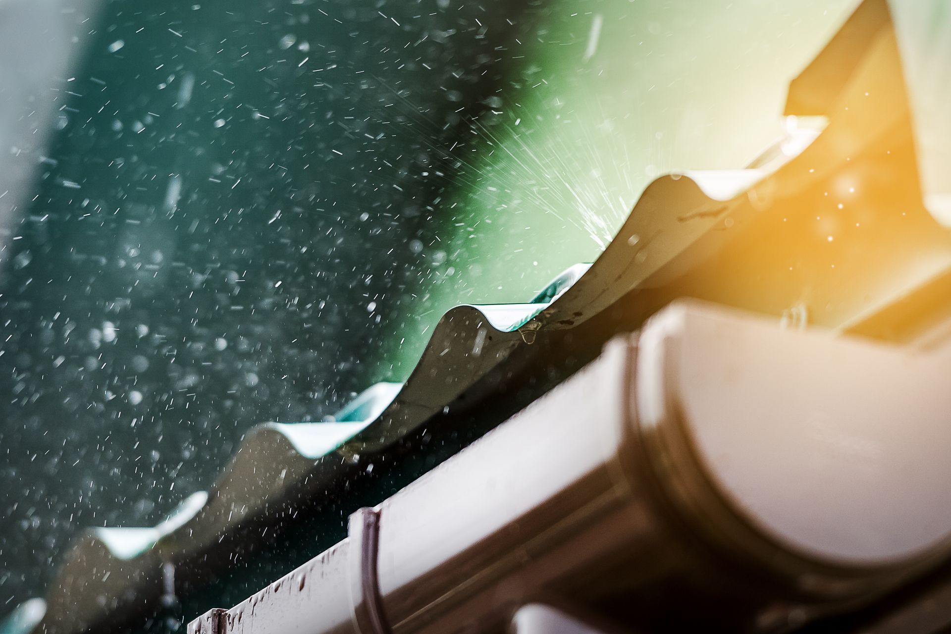A close up of a gutter on a roof with rain falling on it.