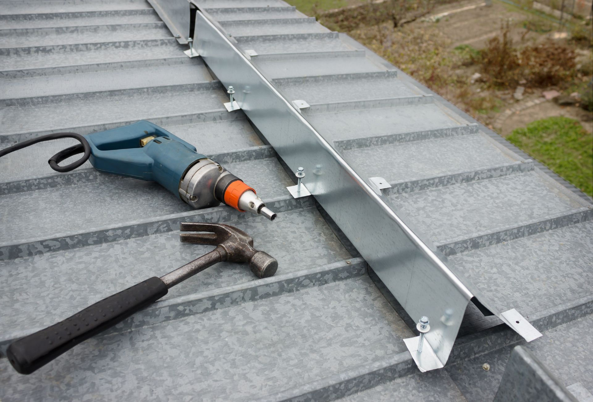 A hammer , drill and screwdriver are sitting on top of a roof.