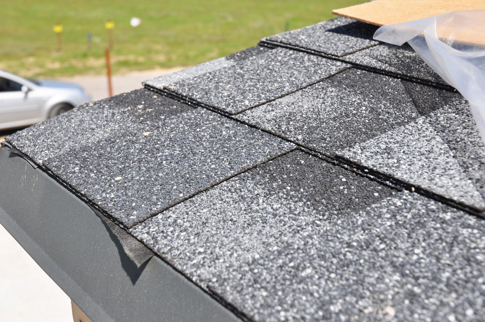 A close up of a roof with shingles and a car in the background
