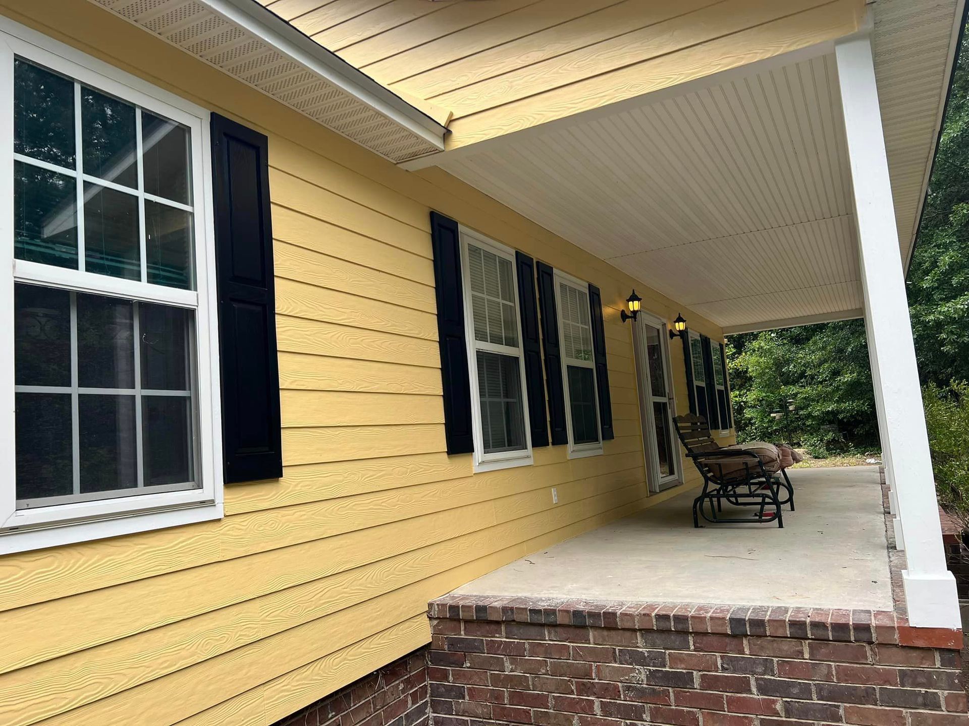 A yellow house with black shutters and a porch