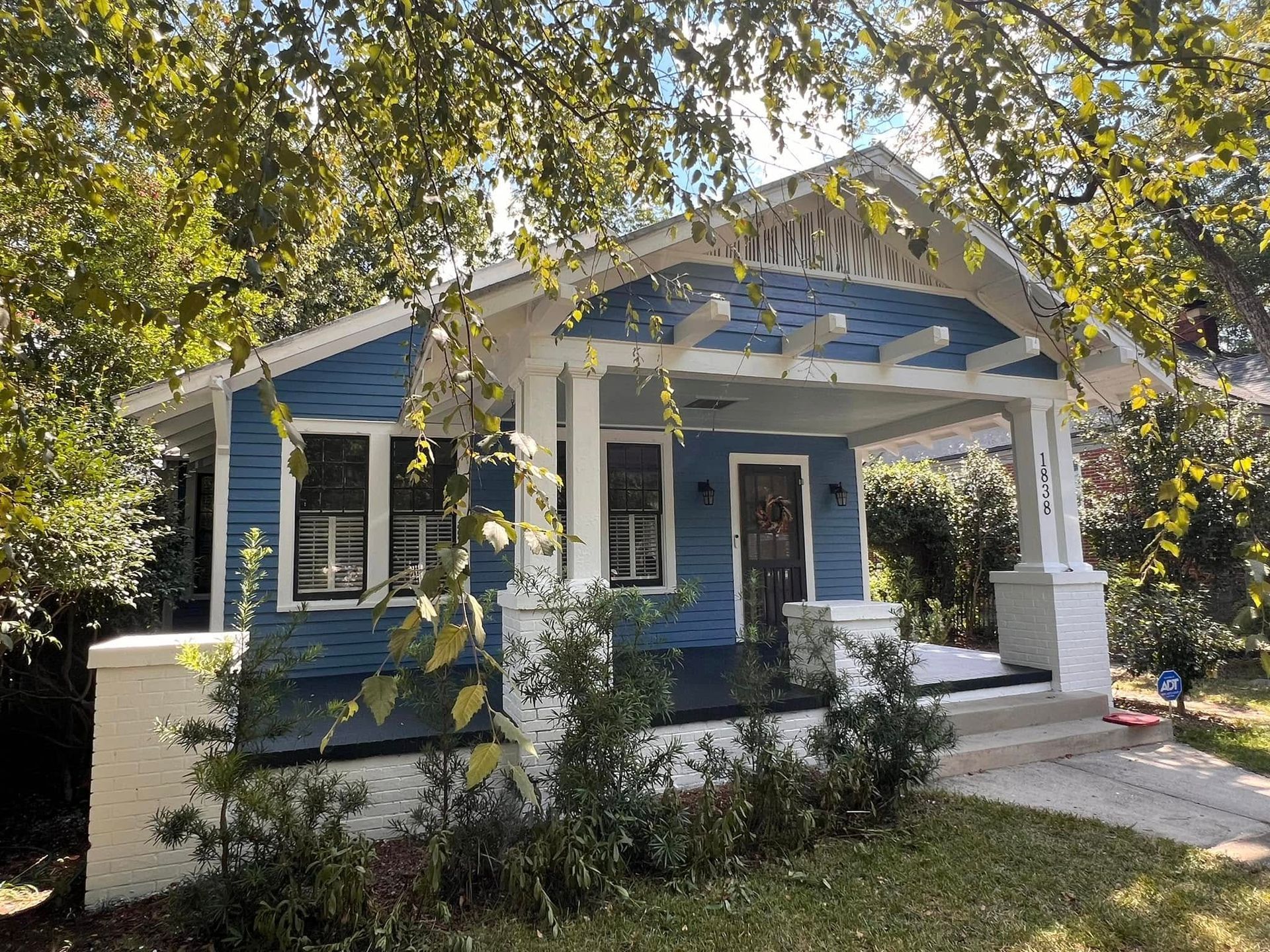 Blue house with white trim, porch, and a lush green yard.