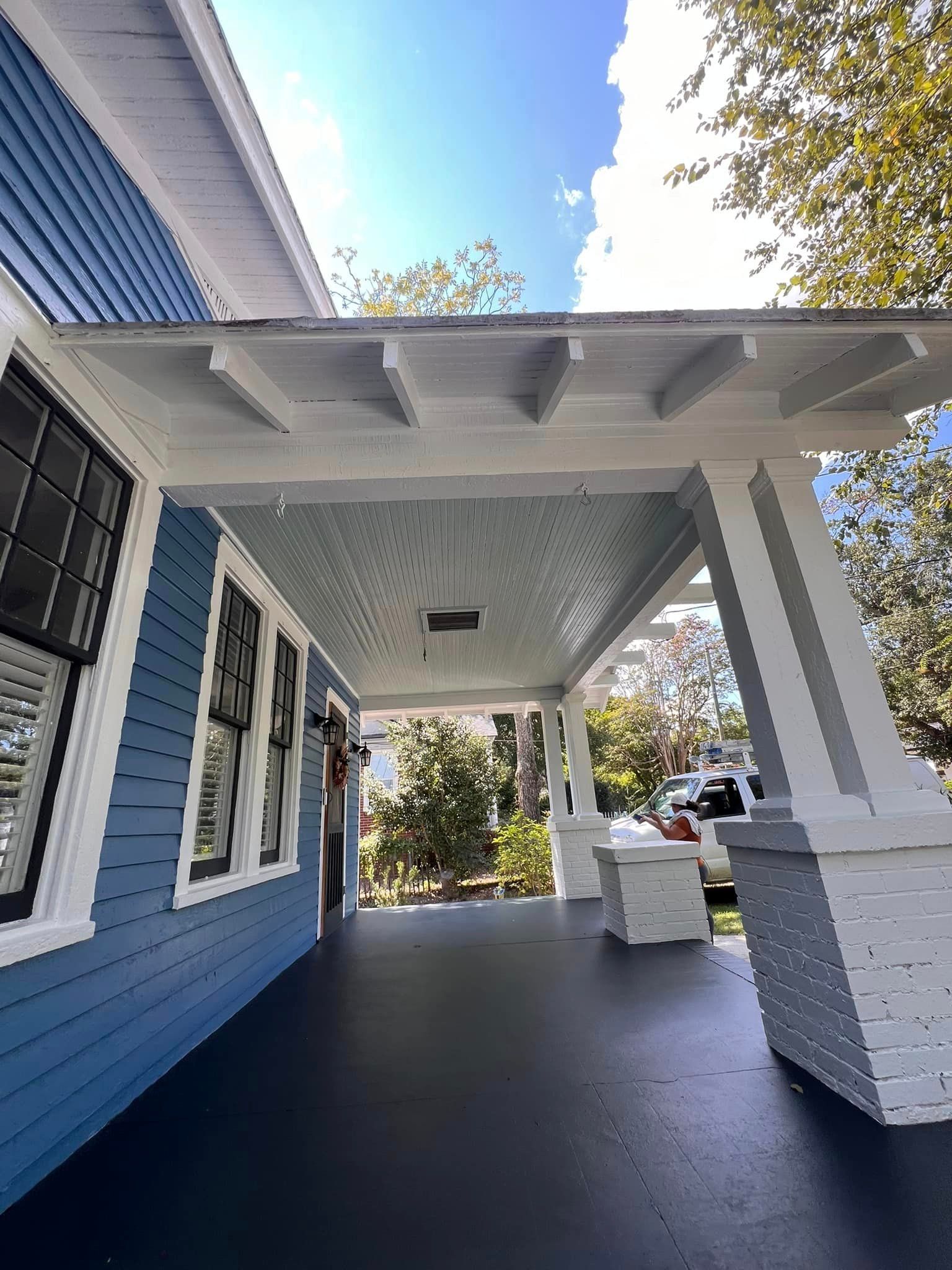 Blue house with a white porch roof, black windows, and gray porch floor.