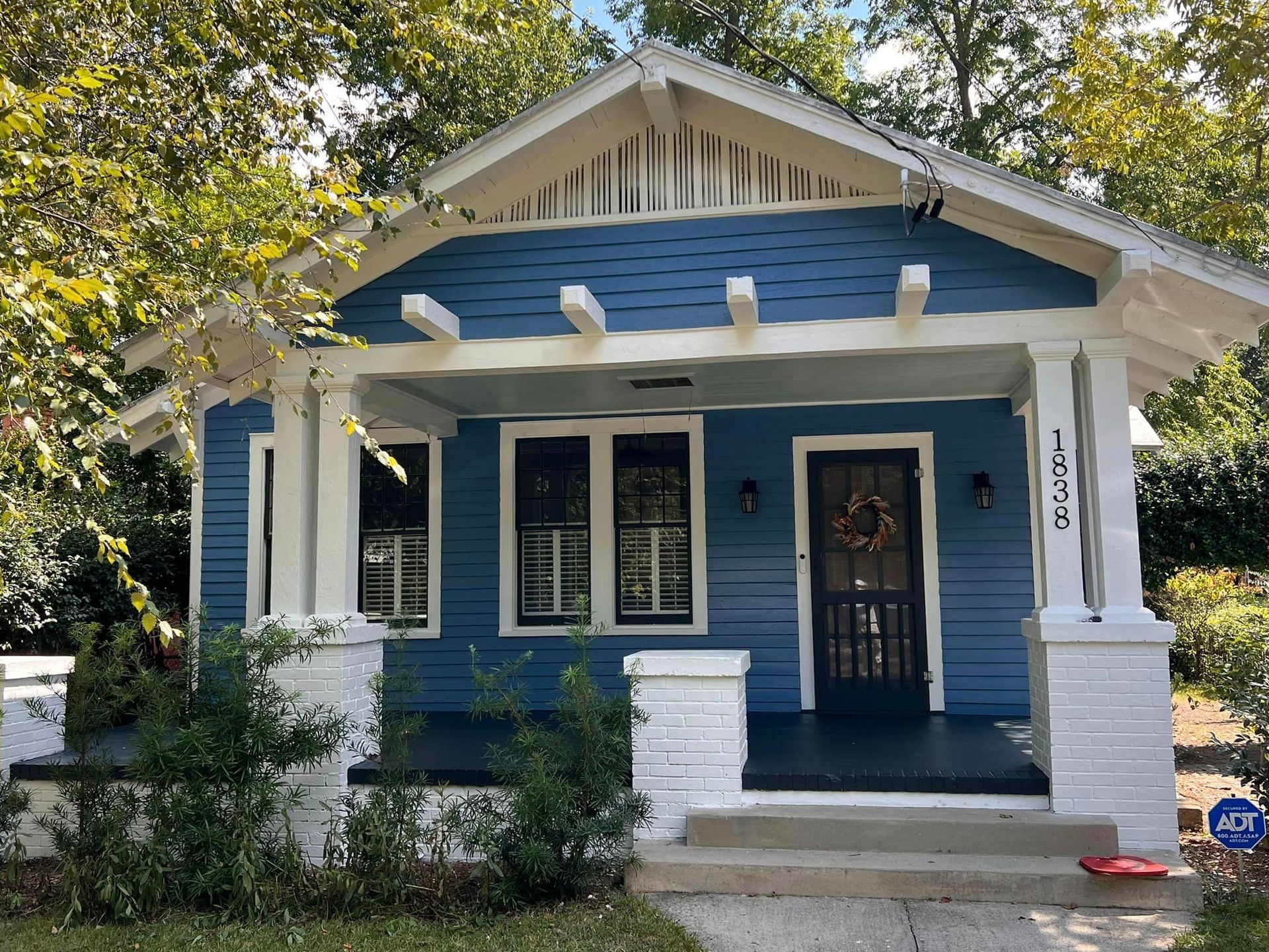 Blue Craftsman-style house with white trim, porch, and door. Bushes are planted along the porch steps.