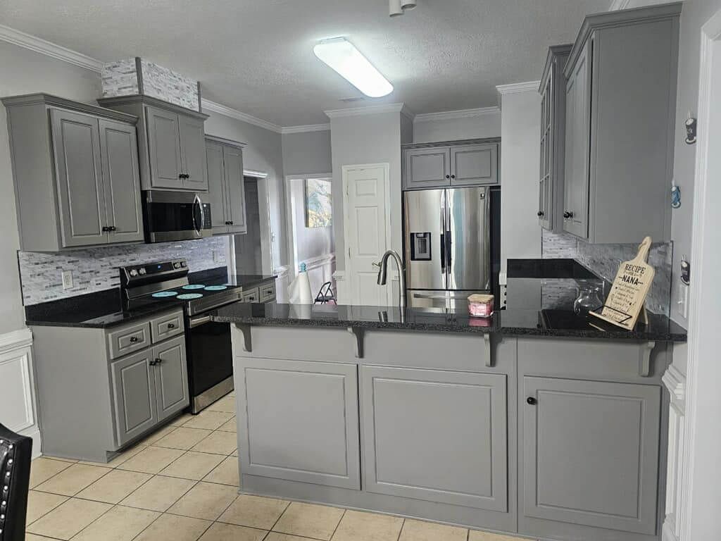 A kitchen with gray cabinets and black counter tops