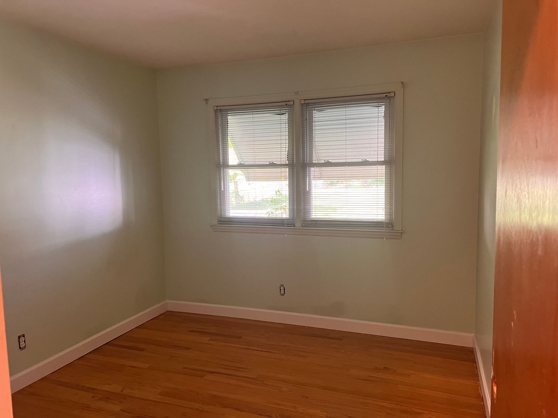 An empty bedroom with two windows and a wooden floor.