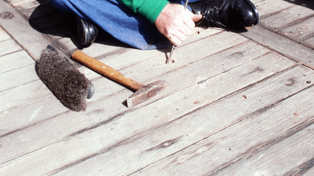 A man is working on a wooden deck with a hammer and brush
