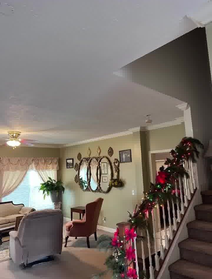 Living room with staircase decorated for Christmas; includes seating, mirrors, and green walls.