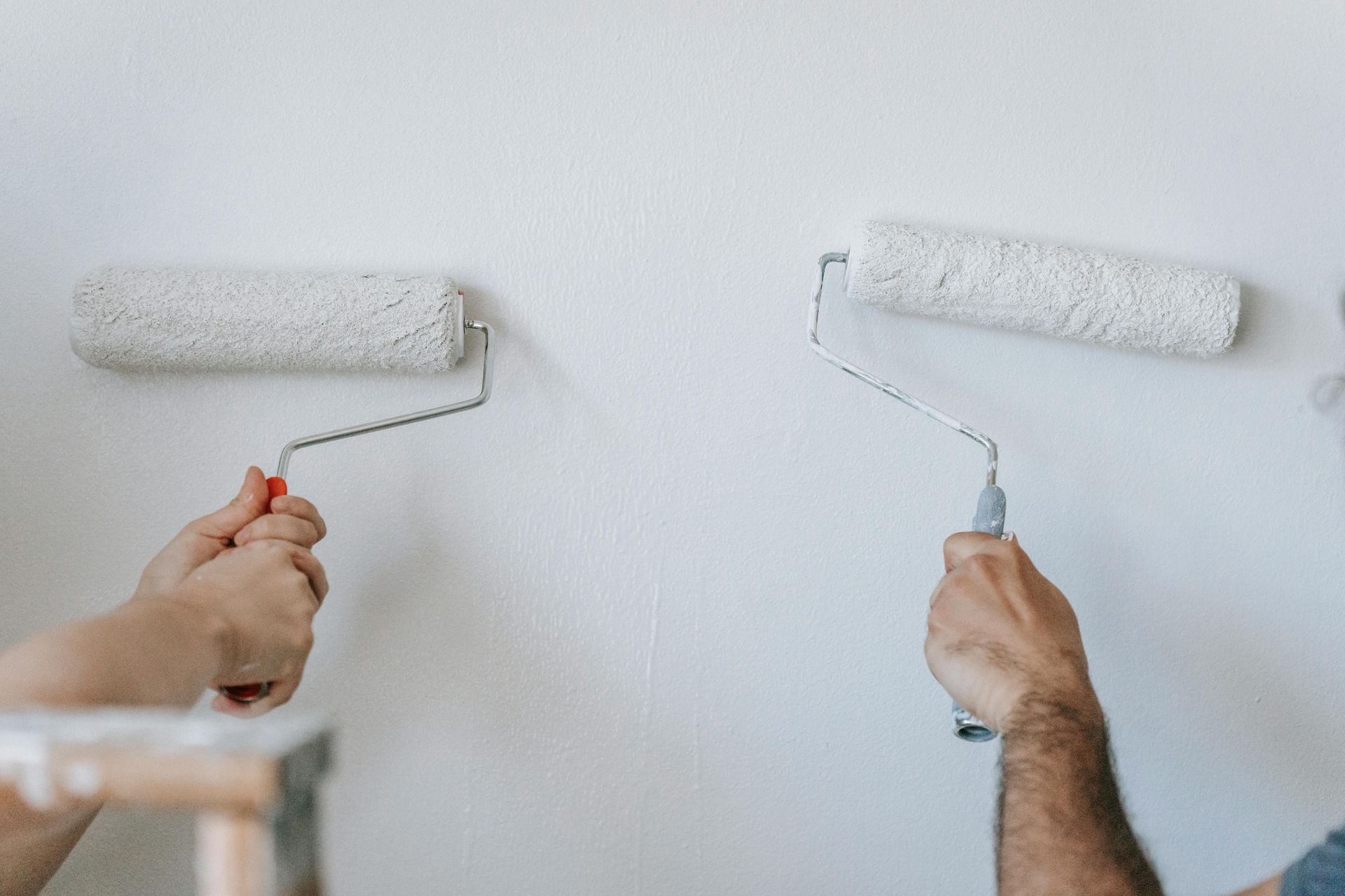 A man and a woman are painting a wall with paint rollers.