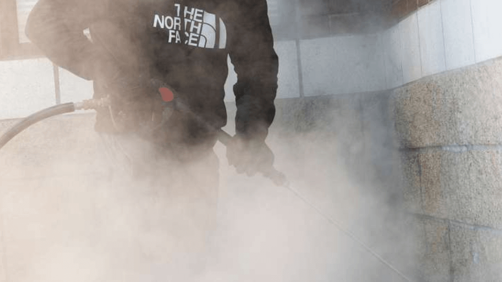 A man in a north face hoodie is cleaning a wall with a hose.
