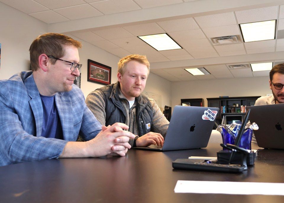 Two men are sitting at a table looking at a laptop computer.