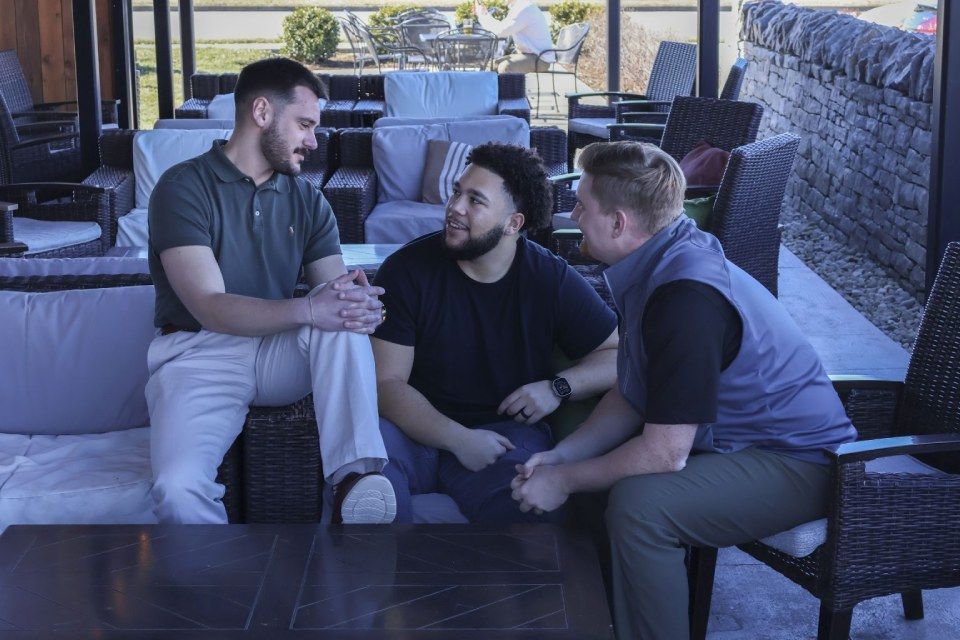 Three men are sitting on a couch talking to each other.