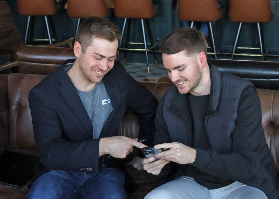 Two men are sitting on a couch looking at a cell phone.