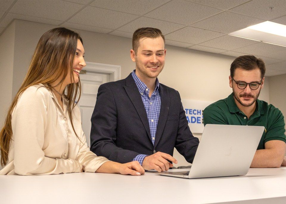 A group of people are standing around a laptop computer.