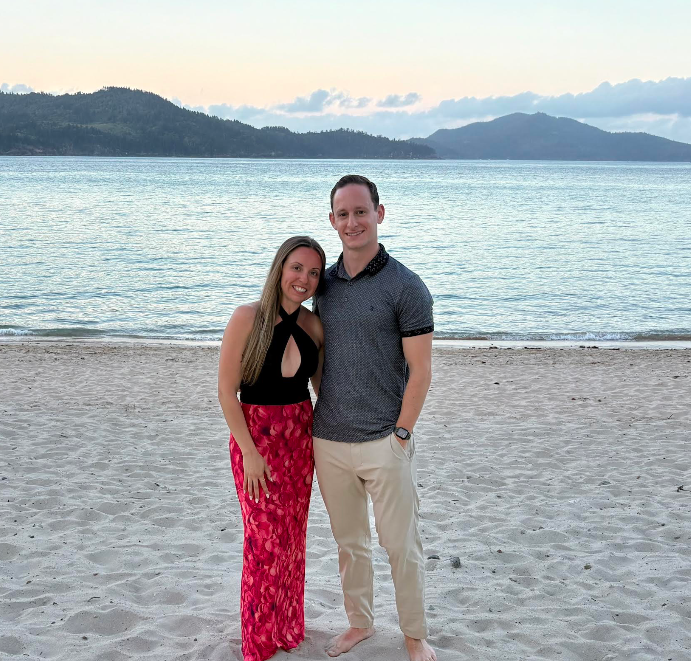 A man drinking water while standing next to a pink flamingo suitcase