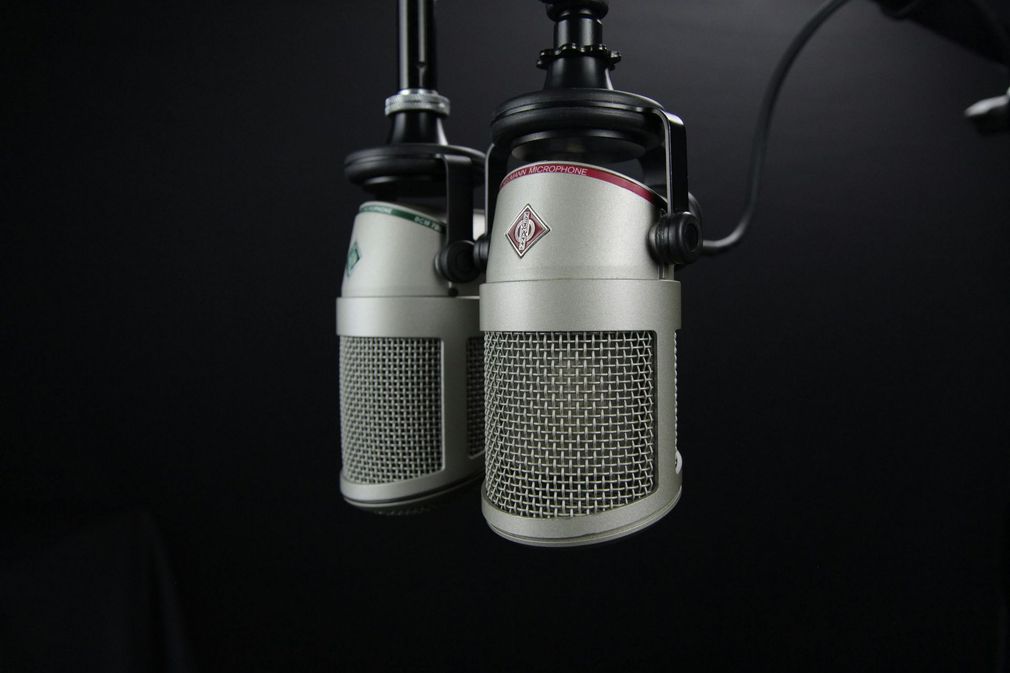 Two microphones are hanging from a stand on a black background.