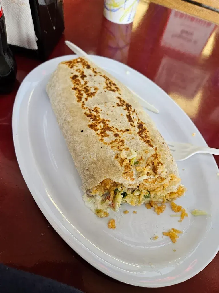 A burrito on a white plate with a fork on a table.