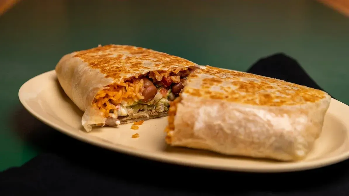 A burrito is cut in half on a plate on a table.