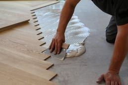 Person installing wood flooring, using a trowel to spread adhesive on the floor.
