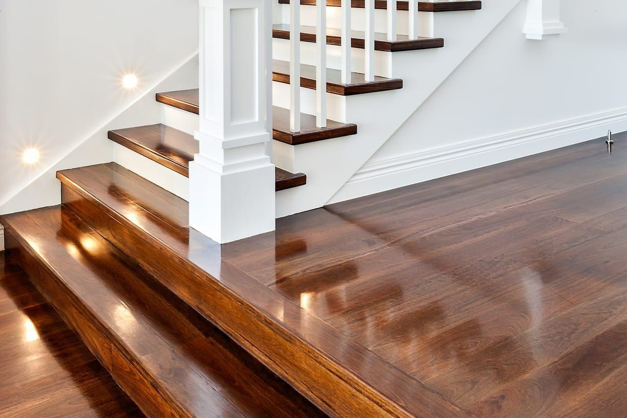 Wooden stairs with glossy finish. White banister and walls. Hardwood floor.