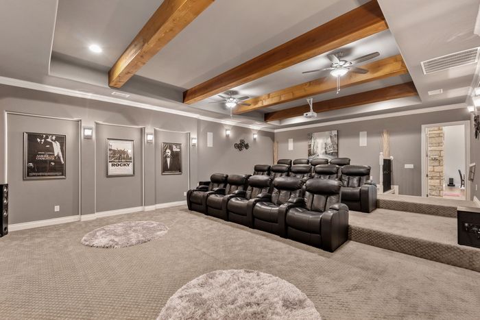 Home theater with tiered seating, gray walls, carpet, and wooden beams.