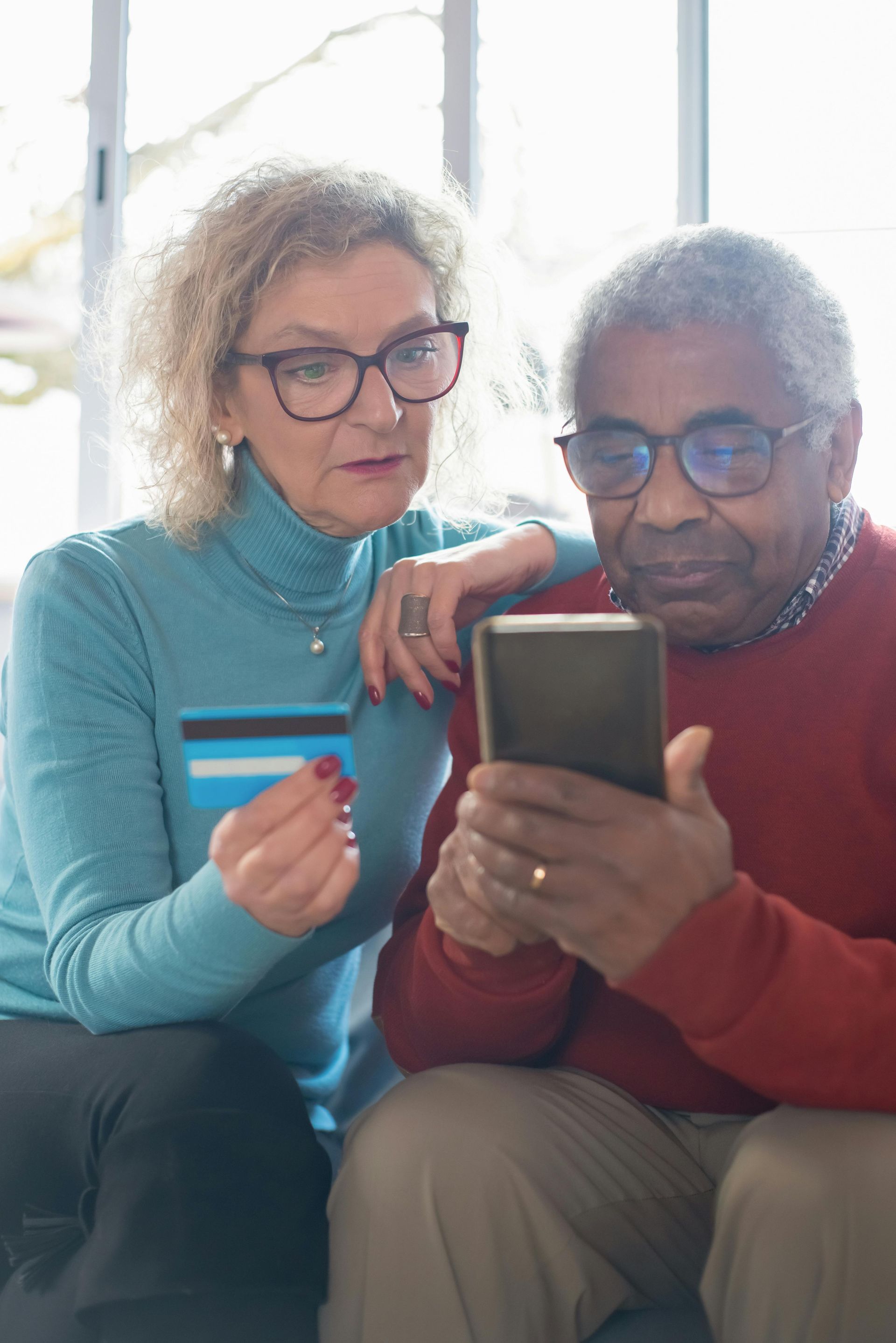 A man and a woman are sitting on a couch looking at a cell phone.