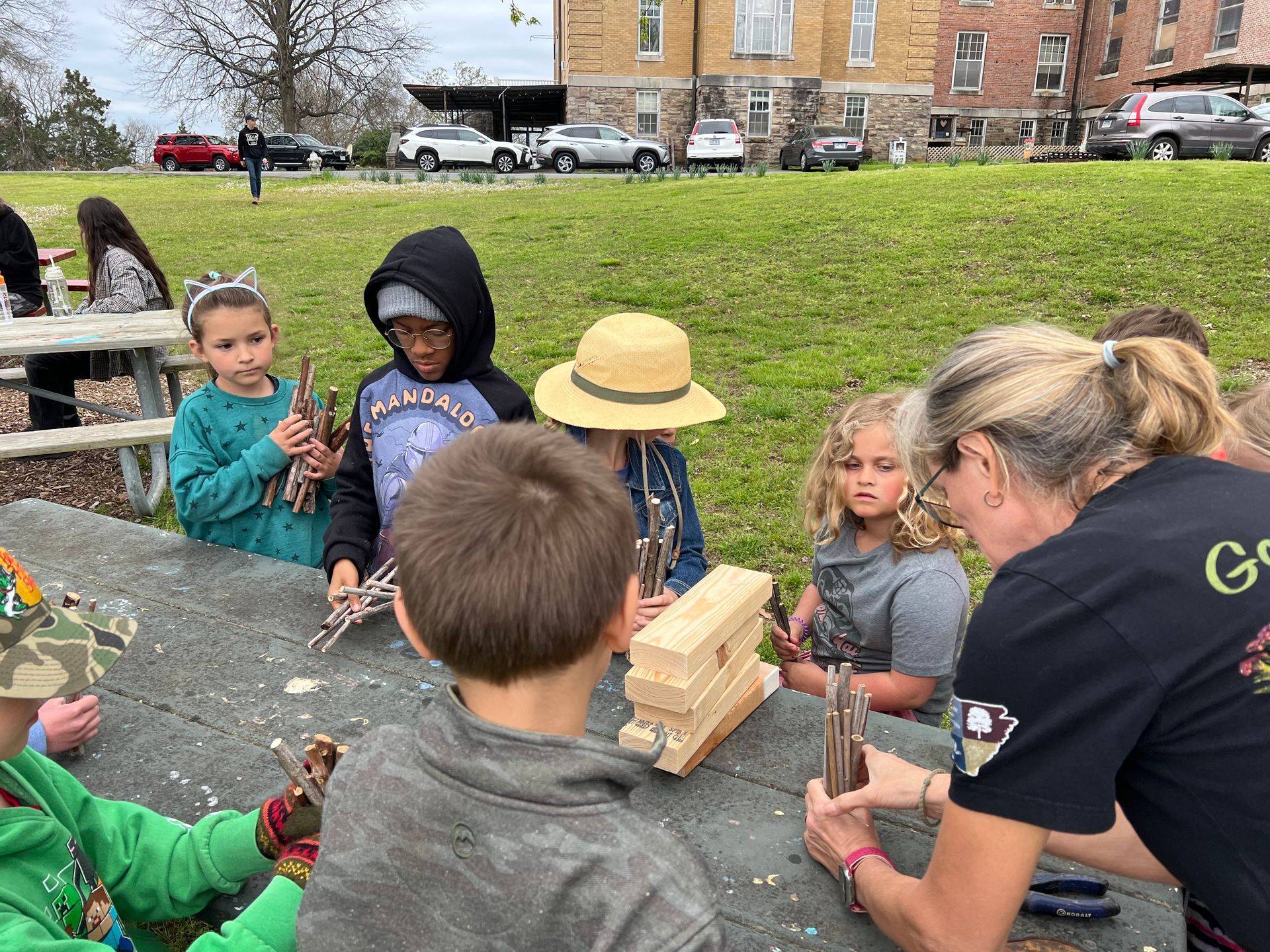 People tending a community garden with raised beds, plants, and a house in the background.