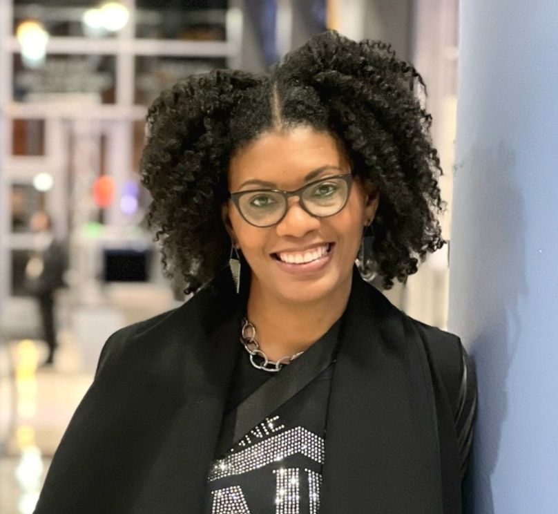 Woman in blue shirt and gloves planting in a garden bed, smiling.