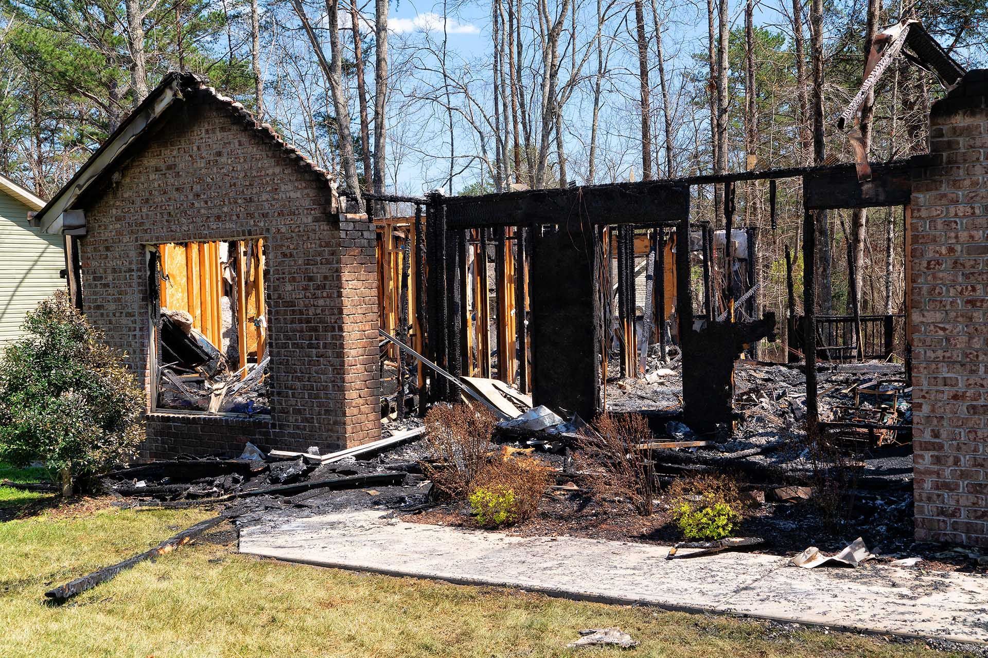 A brick house destroyed by fire; charred remains of walls and structure, debris on the ground.