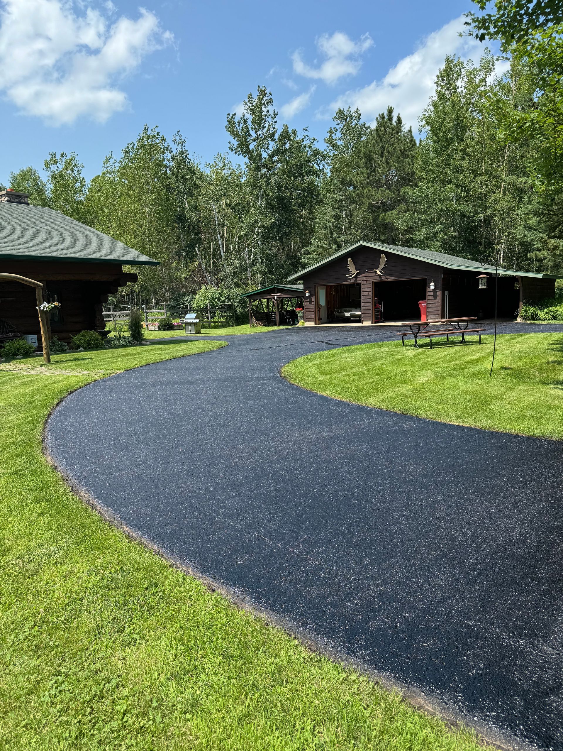 A driveway leading to a house with a picnic table in the grass.