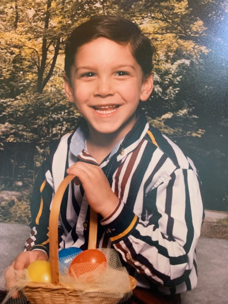 A young boy in a striped shirt is holding a basket of fruit