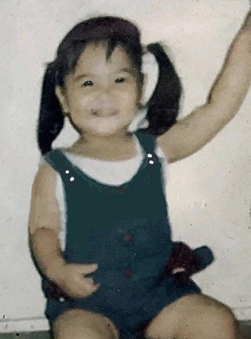 A little girl with pigtails is sitting in front of a white wall.