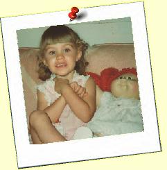 A little girl is sitting on a couch next to a doll.