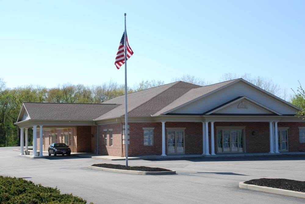 Brick building with an American flag, covered entryway, and a car parked underneath.