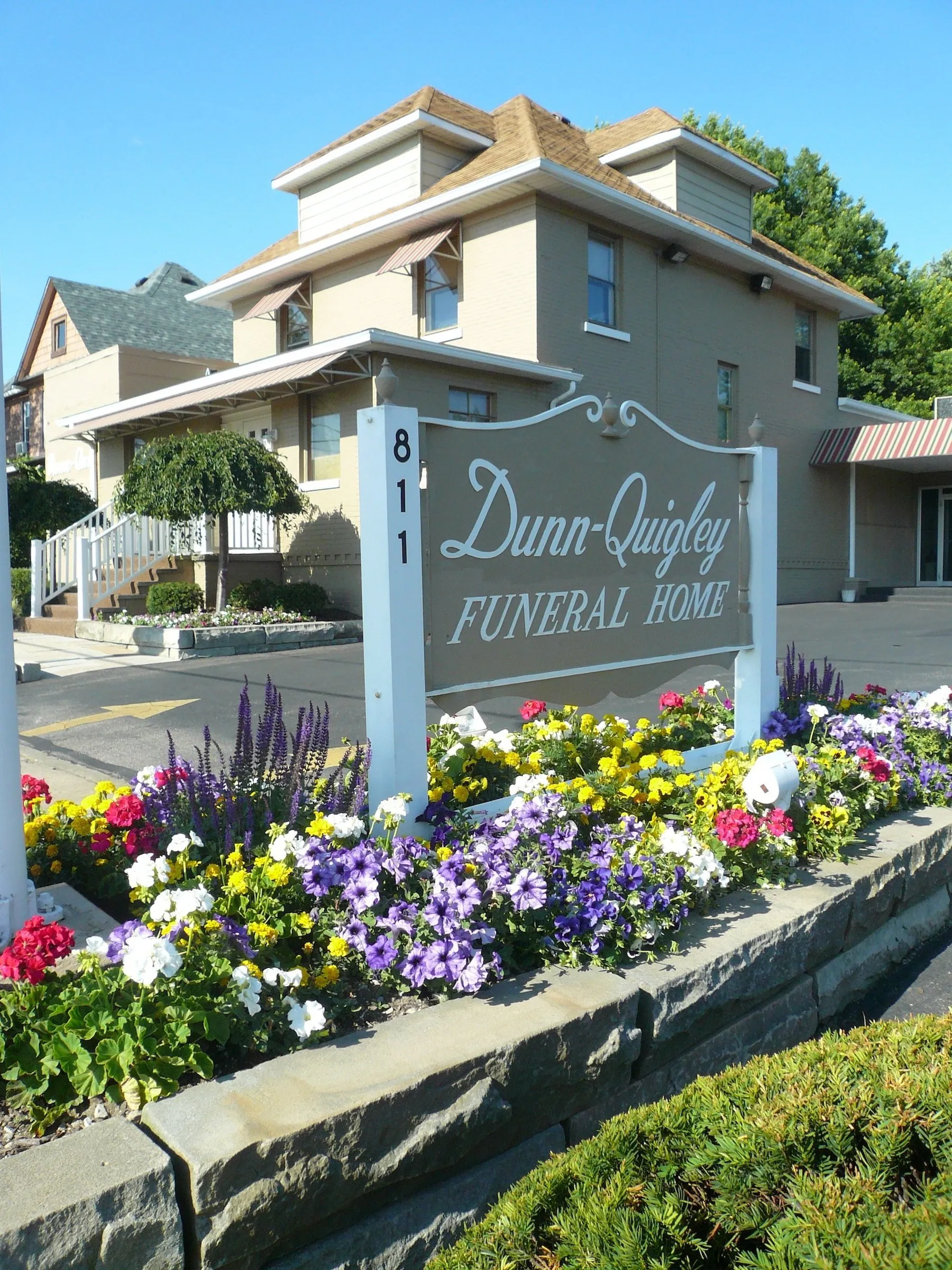 Brick building with covered entrance, small blue car parked out front, green lawn.
