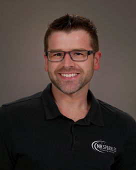 A man wearing glasses and a black shirt is smiling for the camera.