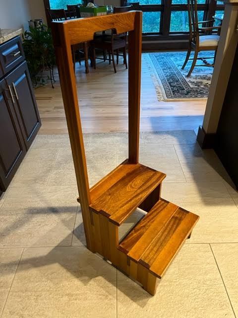 Wooden step stool with two steps and a tall back, indoors.