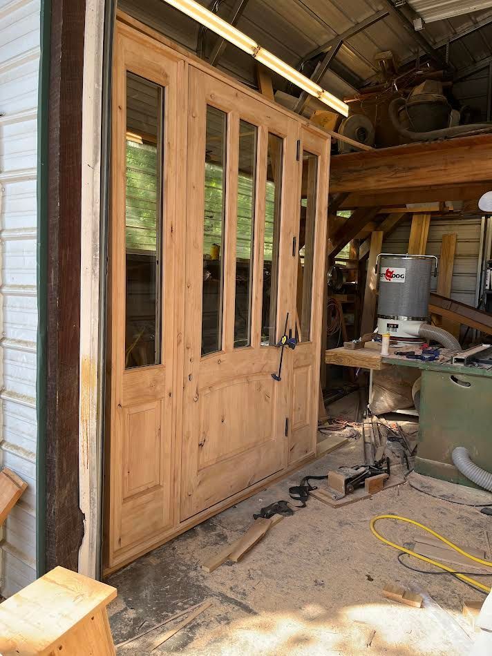 Wooden doors with glass panels, in a workshop setting. Tools and wood scraps surround the doors.