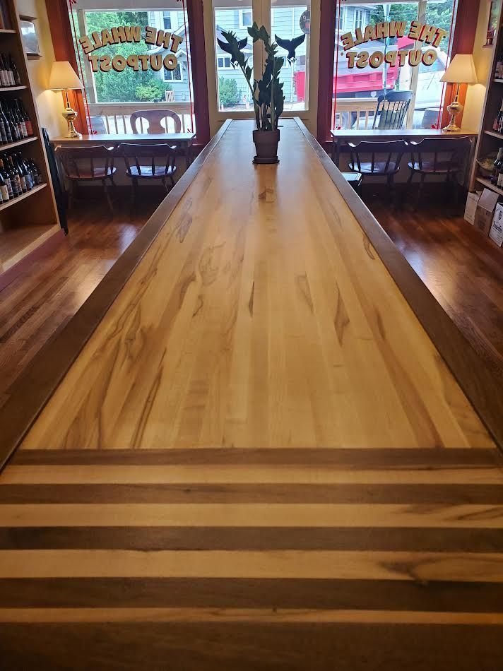 Long wooden counter inside a store, with two windows and a small plant in the middle.