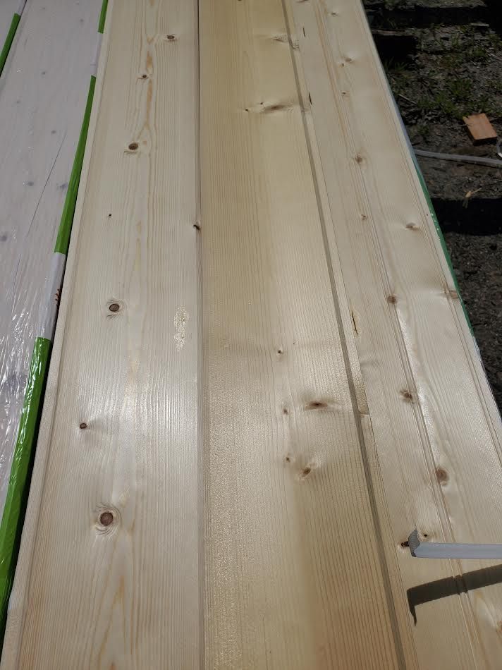 Wooden planks with visible grain and knots, lying outdoors on a green-wrapped base.