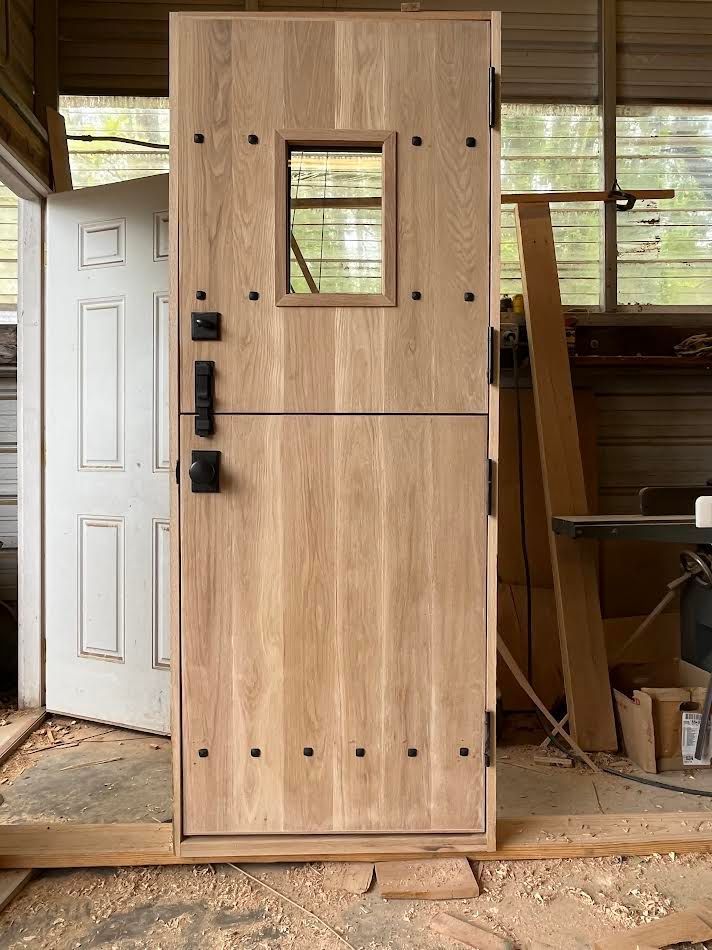 Wooden door with small window and black hardware, in a workshop setting.