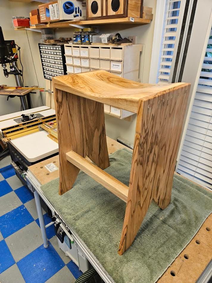 Wooden stool with saddle seat on a workbench in a workshop.
