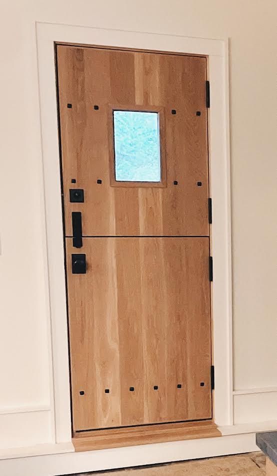 Wooden door with a small window, black hardware, and wood-toned panels set in a white door frame.